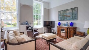 Ein Wohnzimmer mit Sofa, Sessel, Hocker, Fernseher und einem Bild an der Wand.