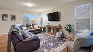 A living room with a sectional sofa, a flat-screen TV, a fireplace, and a large window with blinds. - Fountain Family Retreat | Pet Friendly (Fountain)