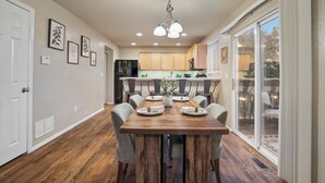 A dining area with a wooden table set for six, surrounded by six chairs. A chandelier hangs above, and there are framed pictures on the wall. - Fountain Family Retreat | Pet Friendly (Fountain)