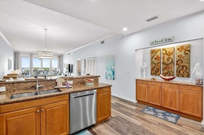 A modern kitchen with granite countertops, stainless steel appliances, wooden cabinets, and a view to the outdoors. - Clearwater Calm Condo, Waterfront (Clearwater Beach)