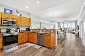 A modern kitchen with wooden cabinets, stainless steel appliances, and a dining area with a view. - Clearwater Calm Condo, Waterfront (Clearwater Beach)
