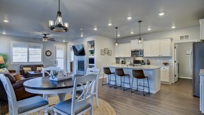 A modern kitchen with white cabinets, a central island with bar stools, a flat-screen TV, and a ceiling fan.