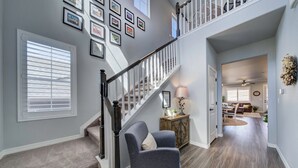 A spacious hallway with a carpeted staircase, a gray armchair, and a dining area with a table and chairs.