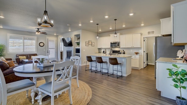 A modern kitchen with white cabinets, a central island with bar stools, a flat-screen TV above the island, and a dining area with a round table and chairs.
