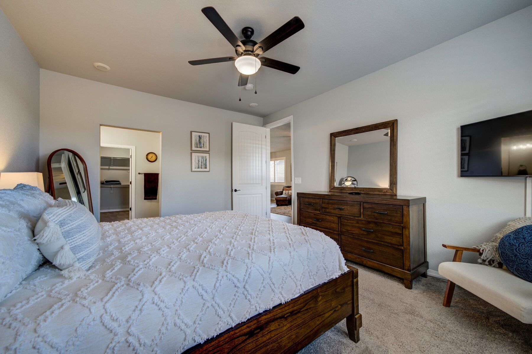 A bedroom with a bed, dresser, vanity, and a ceiling fan.
