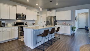 A modern kitchen with white cabinetry, stainless steel appliances, a granite countertop, and a bar area with stools.