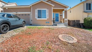 A residential house with a garage, a driveway, and a landscaped front yard with mulch and a fire pit. - The Cozy Oak | Modern Basement Apartment (Fountain)