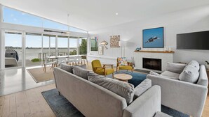 A modern living room with a large sofa, a fireplace, and a view of the water. - Riverside Retreat - Waterfront - Hindmarsh Island (Hindmarsh Island)