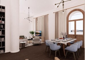 Et moderne spiseområde med et stort bord dækket til seks personer, omgivet af lyseblå stole. En reol og en sofa ses i baggrunden.