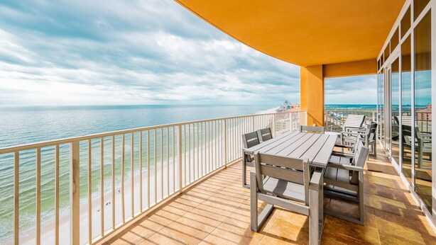 Ein Balkon mit Holztisch und -stühlen mit Blick auf einen Strand und das Meer.