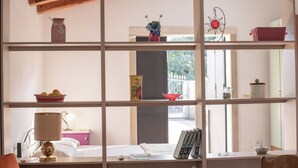 A room with a wooden bookshelf, a desk with a lamp, and a view of the outdoors through a window. - Monasteri Rural Holiday Home (Sicilia)