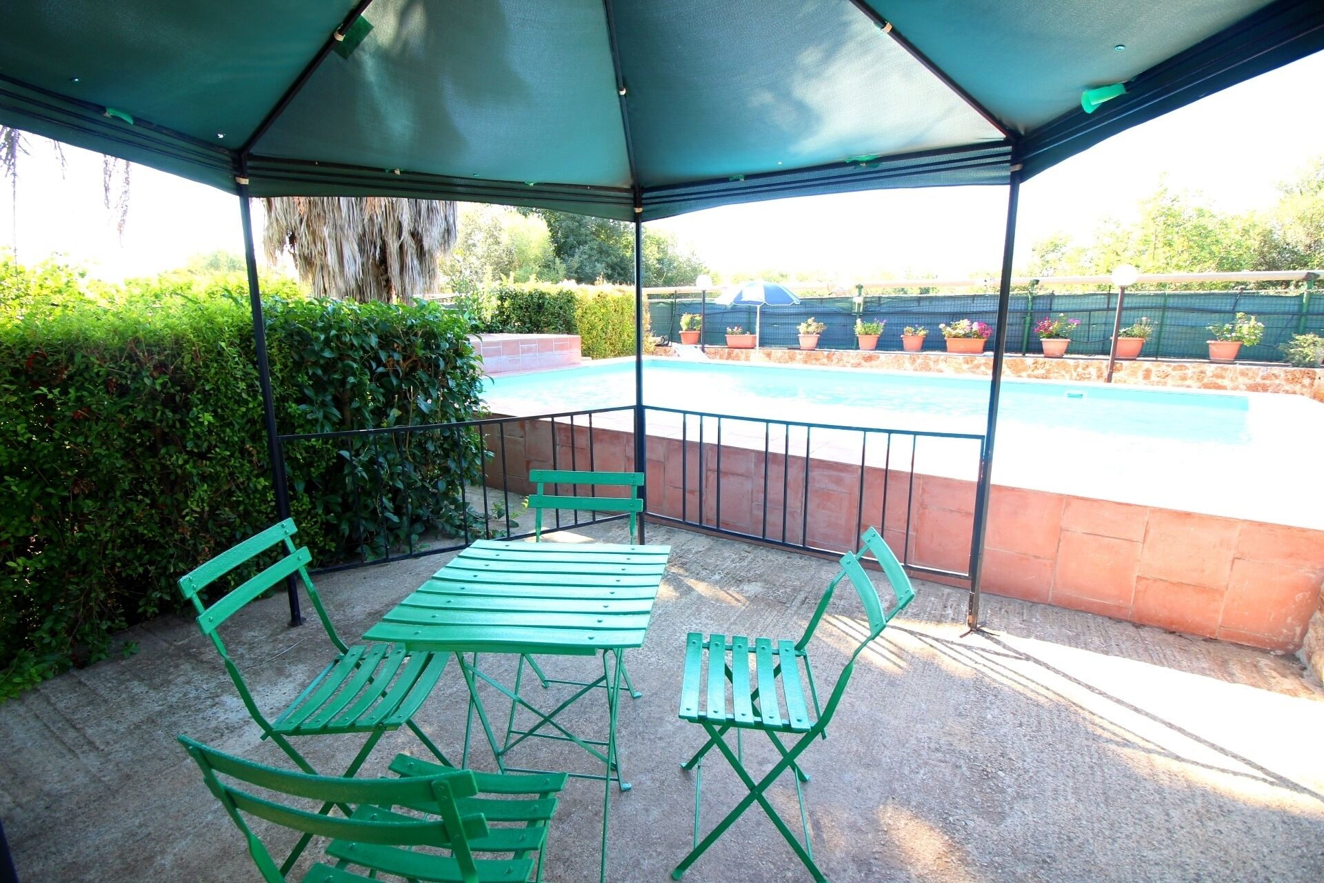Zona de porxo coberta amb piscina, moble metàl·lic verd i plantes en testos.