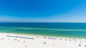Ein Strand mit Reihen aus blauen Sonnenschirmen und Liegestühlen, einem wolkenlosen, blauen Himmel und ruhigem Meer.