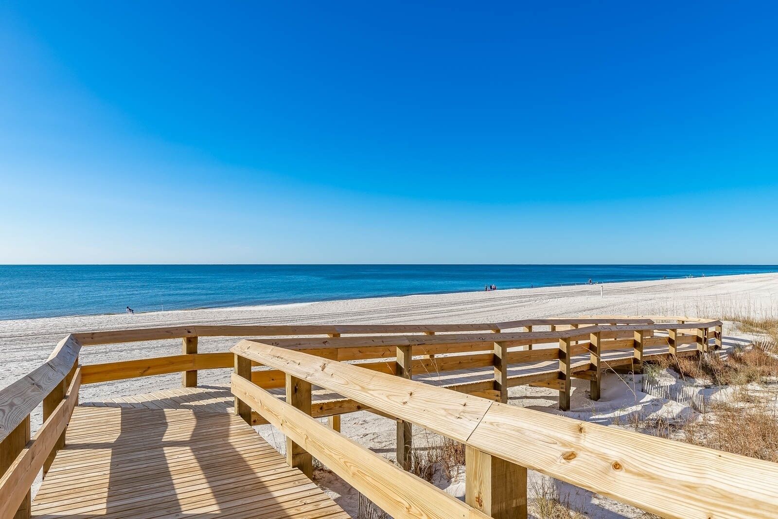A wooden boardwalk leading to a sandy beach with a clear blue sky.