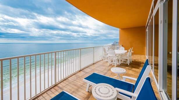 Un balcón con vistas al mar, sillas blancas y una mesa.