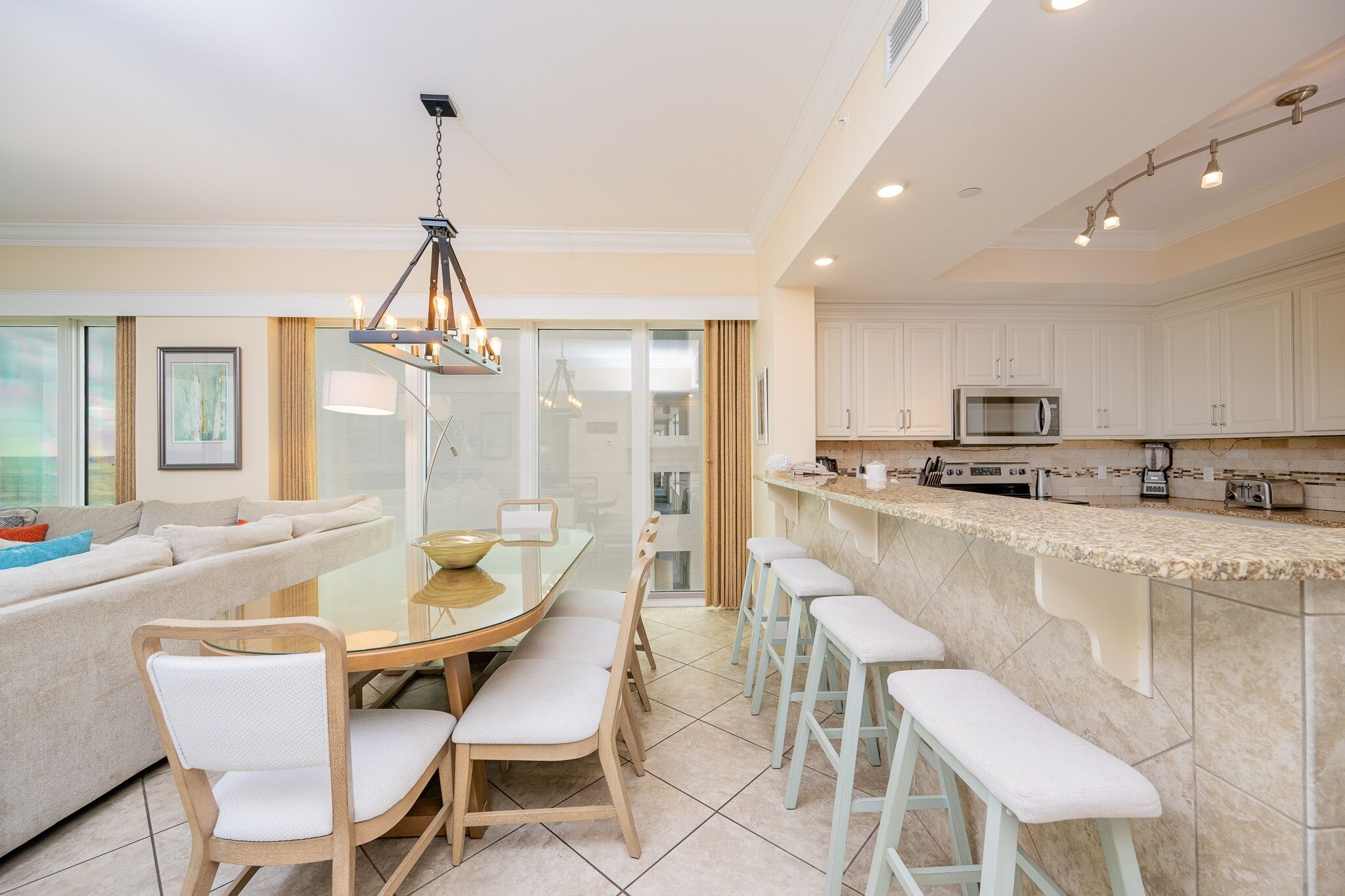 A modern kitchen with white cabinets, a central island with stools, and a dining area with a glass table and chairs.