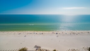 A beach with a clear sky, calm sea, and a sandy shore with people and umbrellas. - Phoenix Orange Beach 1701 4 Bedroom Condo (Orange Beach)