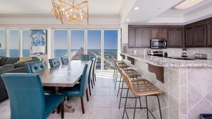 A spacious dining area with a view of the city, a modern kitchen with dark cabinets, and a large chandelier. - Phoenix Orange Beach 1701 4 Bedroom Condo (Orange Beach)