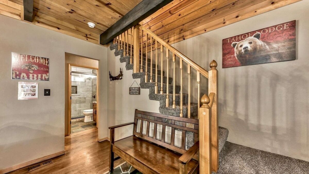 A wooden staircase with a bench at the bottom, a bear-themed wall art, and a welcome sign.