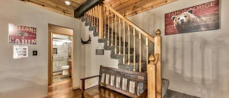 A wooden staircase with a bench at the bottom, a bear-themed wall art, and a welcome sign.