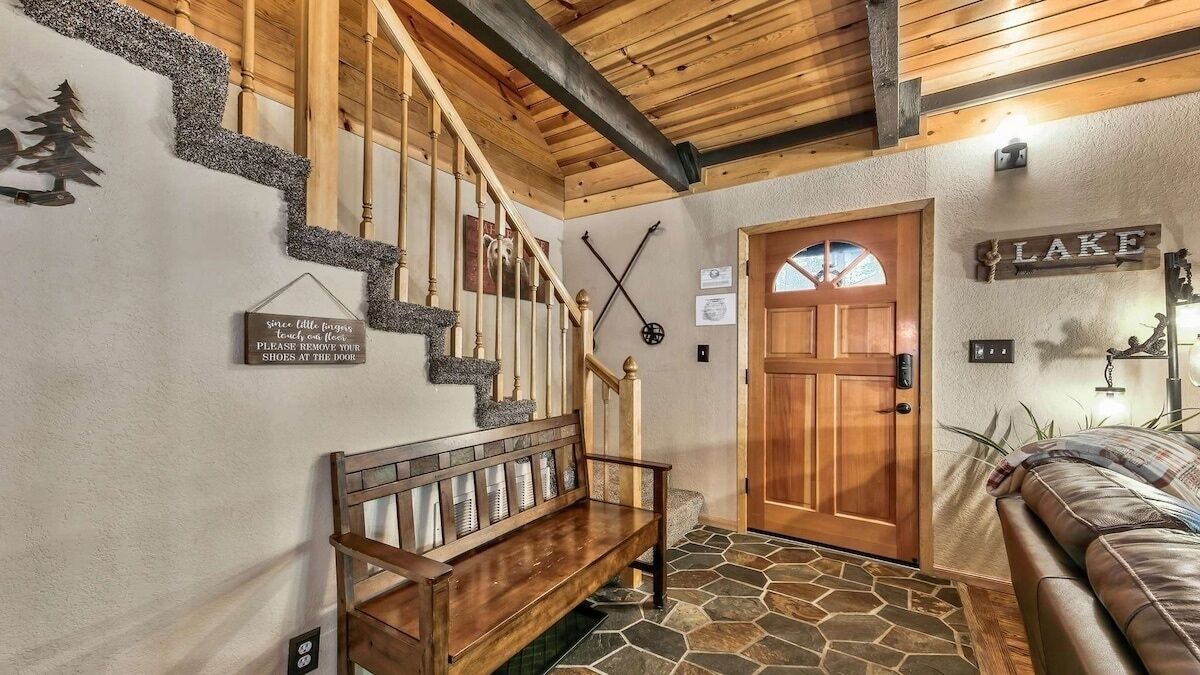 Eine Holztreppe mit einer Steinsäule, einer hölzernen Bank, einer mit 'SEE' beschrifteten Tür und einem Schild an der Wand.