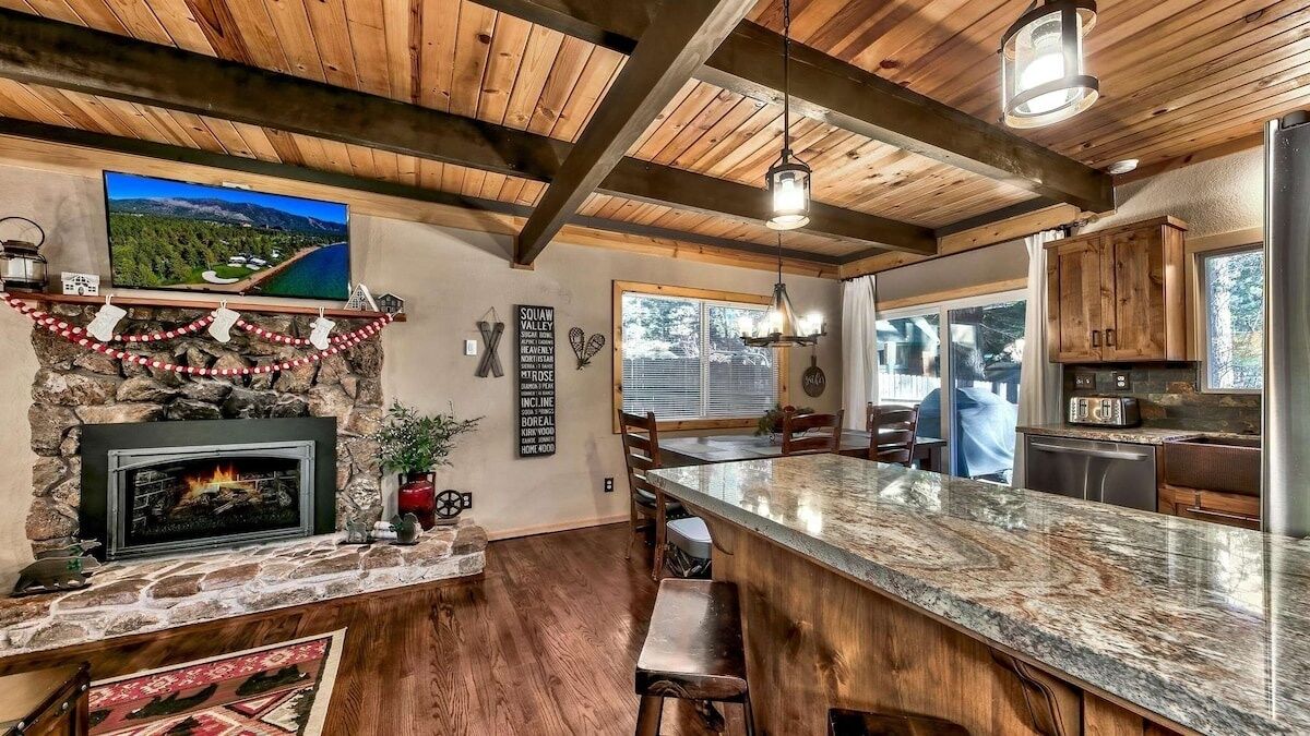 A rustic kitchen with a stone fireplace, wooden beams, and a large island counter.