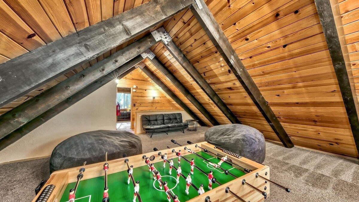 Una habitación en el ático con una mesa de fútbol, un sofá y una chimenea.