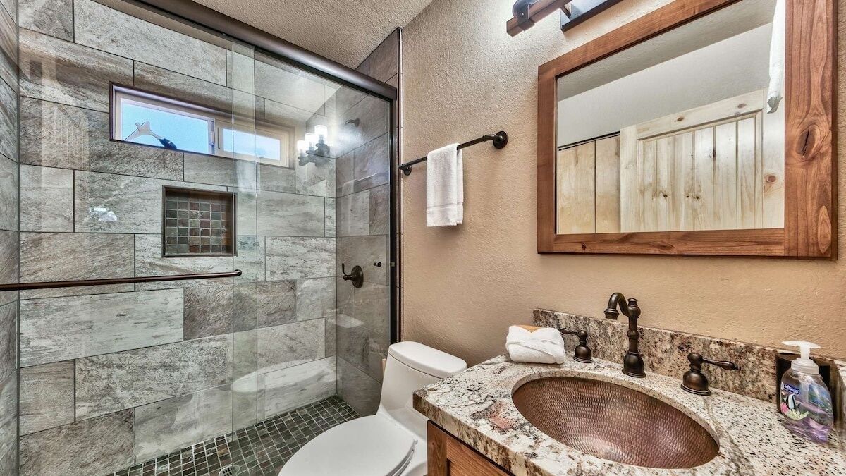 A bathroom with a glass-enclosed shower, a marble sink, and a wooden vanity.