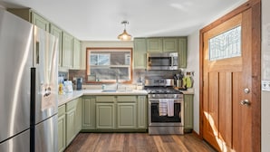 Een keuken met groene kasten, roestvrijstalen apparatuur, een houten deur en een raam met uitzicht.