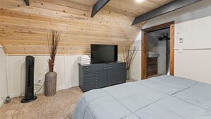 Een slaapkamer met een bed, een dressoir, een televisie en een ventilator.
