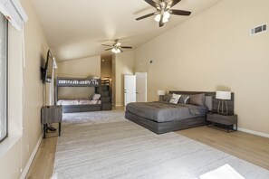 A bedroom with a large bed, a smaller bed, a desk, a chair, a ceiling fan, and a window.