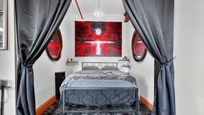 Un dormitorio con cama, cortinas, un cuadro colgado en la pared y una mesita de noche.