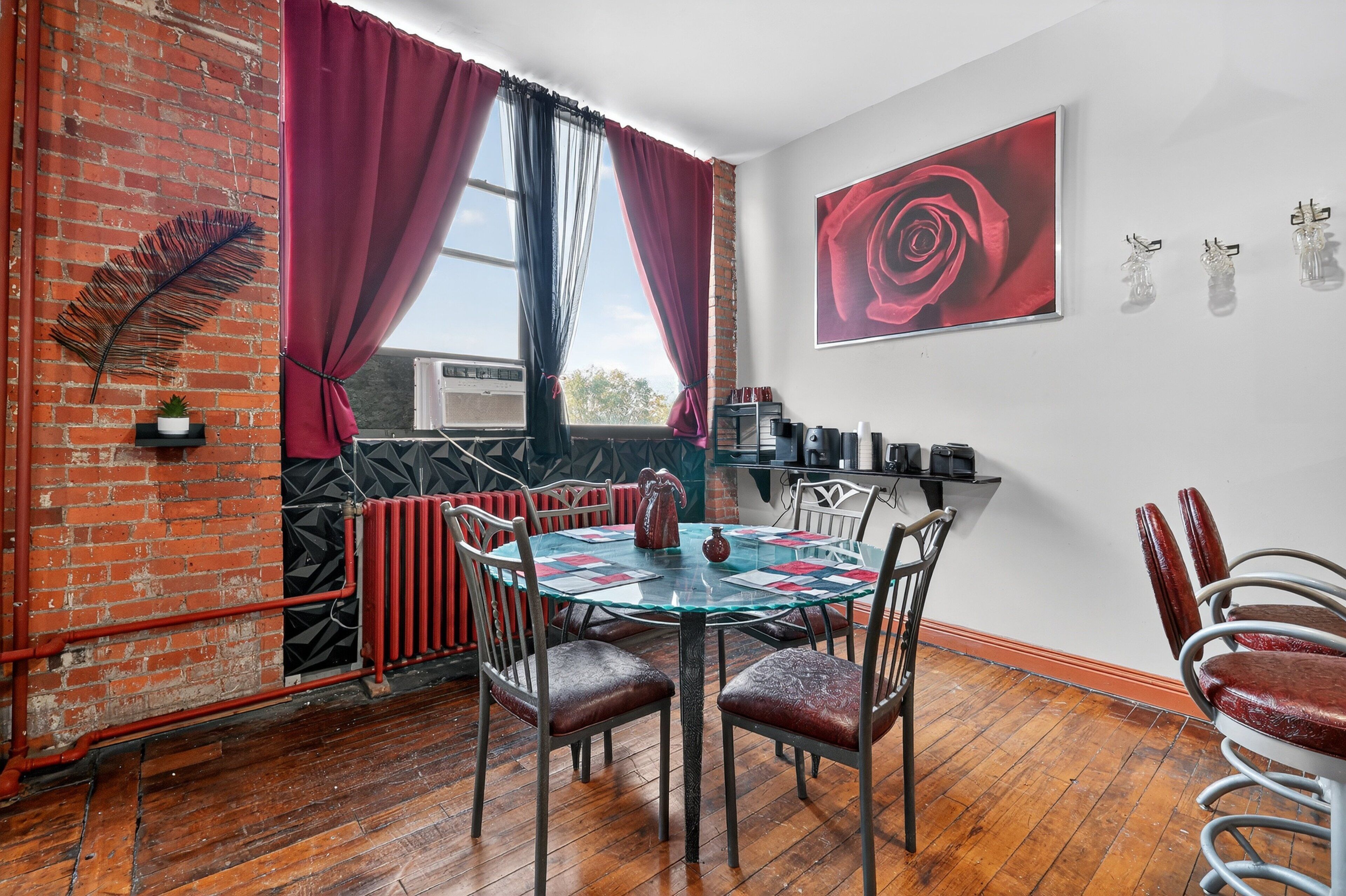 Un comedor con una mesa de vidrio, cortinas rojas y un cuadro de una rosa roja.