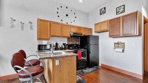 Una cocina compacta con armarios de madera, un refrigerador negro, un microondas y una pequeña isla con un lavamanos y taburetes.