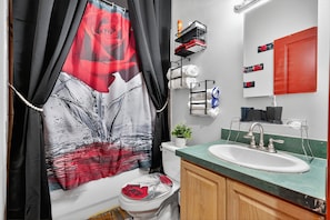 Ein Badezimmer mit Duschvorhang mit rotem Rosenmuster, Toilette, Waschbecken mit grüner Arbeitsplatte und Spiegel mit rotem Schrank.