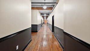 Un pasillo largo y estrecho con suelo de madera y detalles negros, que conduce a una puerta al final.