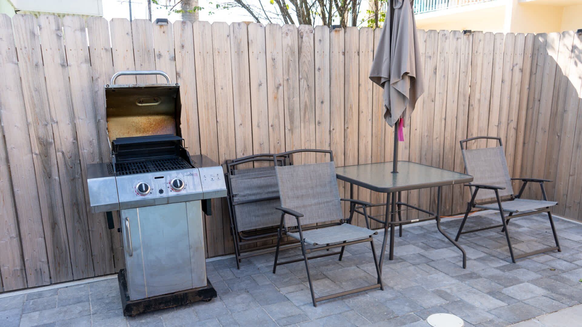 An outdoor patio with a stainless steel grill, two chairs, and a table.