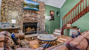 A cozy living room with a stone wall, fireplace, comfortable seating, and a staircase. - Smoky Mountain Bliss 2 Bedroom Cabin (Gatlinburg)