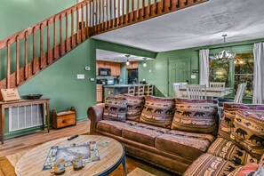 A cozy living room with a brown sofa, a coffee table, and a staircase. - Smoky Mountain Bliss 2 Bedroom Cabin (Gatlinburg)