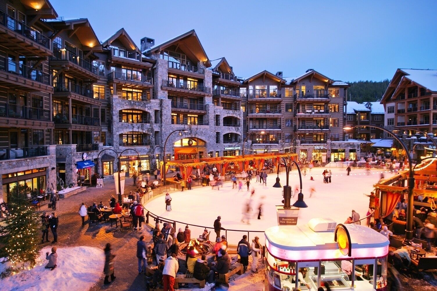 Ein mehrstöckiges Hotel mit Balkonen, einem zentralen Innenhof mit Eislaufbahn und Außenbereichen mit Sitzgelegenheiten.
