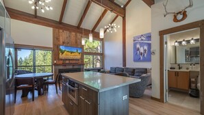 A modern kitchen with wooden cabinetry, a central island, and a dining area with a view of the outdoors. - Indian Hills 6021 2 Bedroom Townhouse (Truckee)