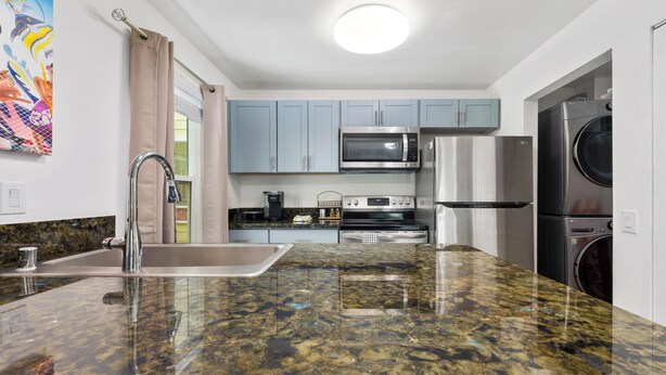 A modern kitchen with granite countertops, stainless steel appliances, and light blue cabinets. - Big Island Fairway Terrace I-208 1 Bedroom Condo (Waikoloa)