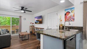 A modern kitchen with a granite countertop, stainless steel appliances, and a dining area with a wooden table and chairs. - Big Island Fairway Terrace I-208 1 Bedroom Condo (Waikoloa)