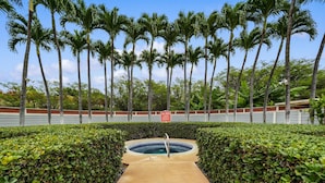 A pool area surrounded by neatly trimmed hedges and tall palm trees. - Big Island Fairway Terrace I-208 1 Bedroom Condo (Waikoloa)