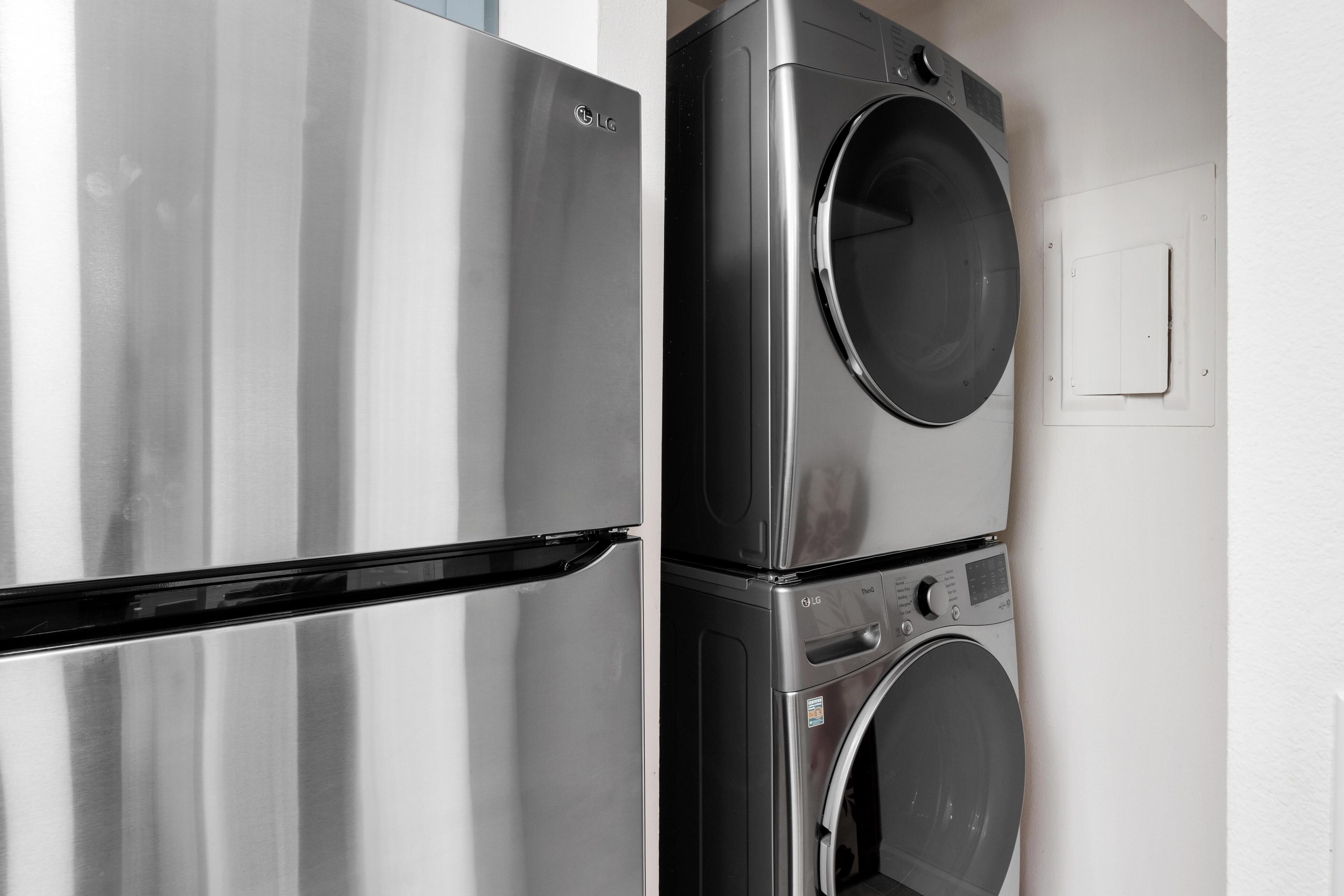 Een koelkast van roestvrij staal en een gestapelde wasmachine en droger in een keuken.