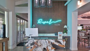 Een receptiebalie met een neonbord waarop 'River CLUB' staat en een glazen vitrine met een houten sculptuur.