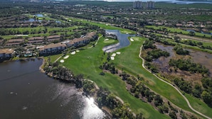 Luchtbeeld van een golfbaan met waterpartijen, woonwijken en hoge gebouwen op de achtergrond.
