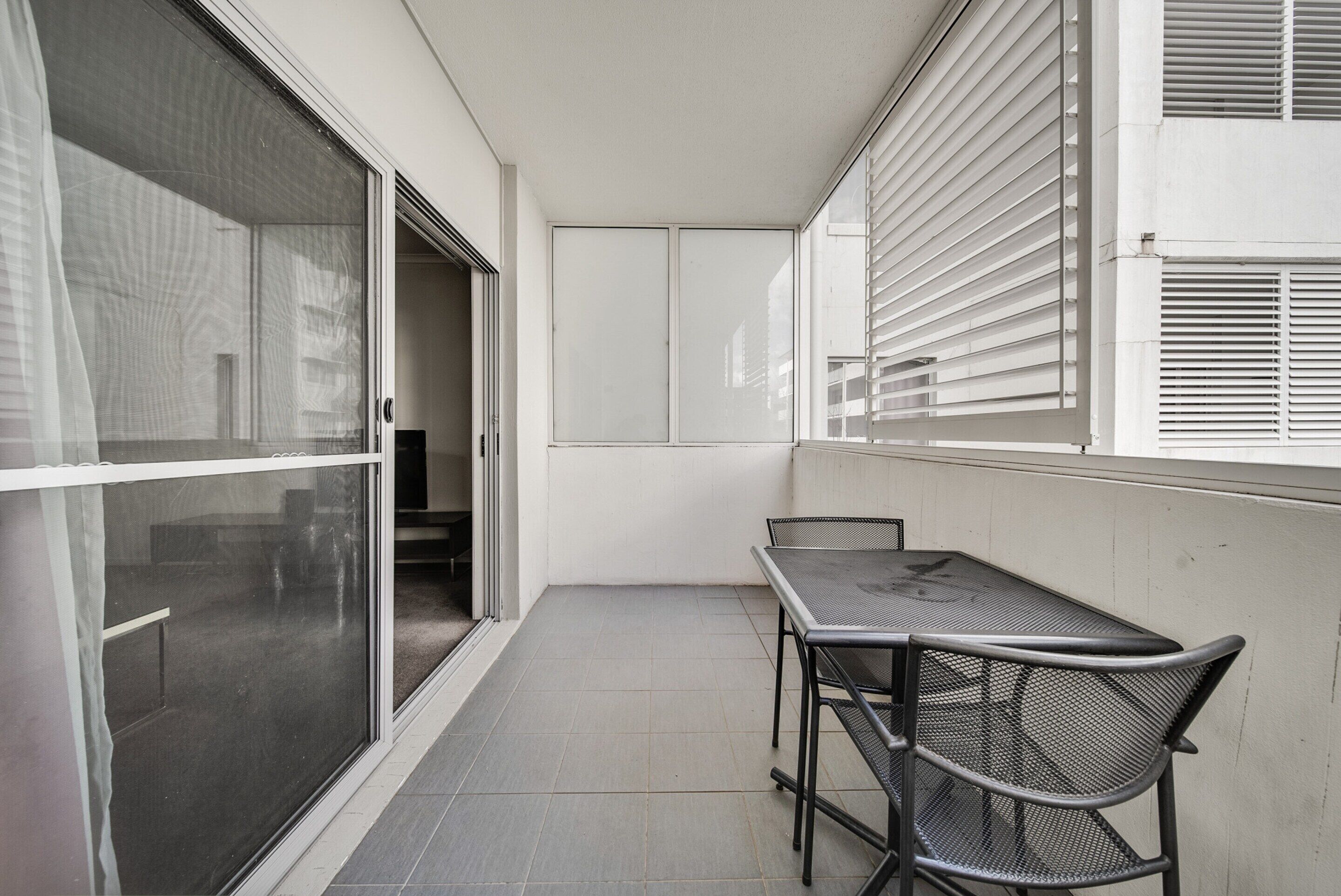 Ein Balkon mit Tisch und Stühlen, eine Schiebeglastür und ein Fenster mit Jalousien.