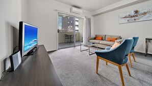 Een moderne woonkamer met een flatscreen televisie, een bank en twee blauwe fauteuils.