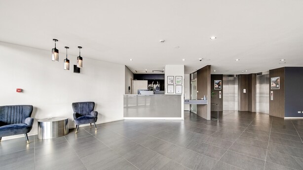 Een moderne lobby met een receptiebalie, twee blauwe fauteuils en een klein bijzettafeltje.